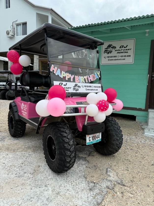 Hot pink golf cart decorated with Happy Birthday banner and pink white balloon clusters at OJ Golf Cart Rentals in San Pedro Belize